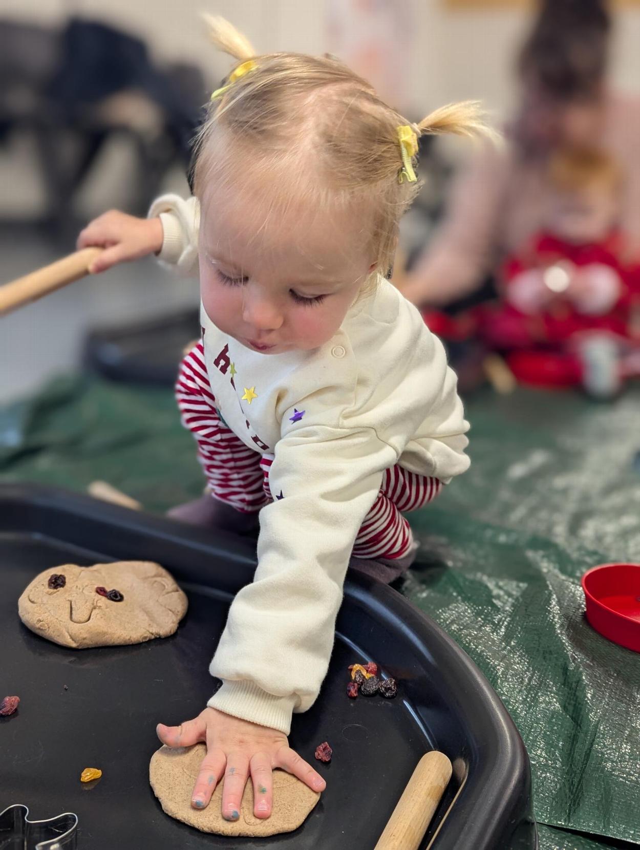 A toddler squishes play dough with her hand.
