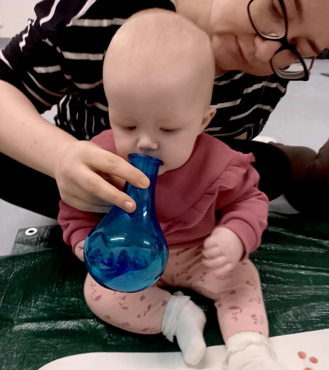 A baby is smelling inside a blue smelling bottle.